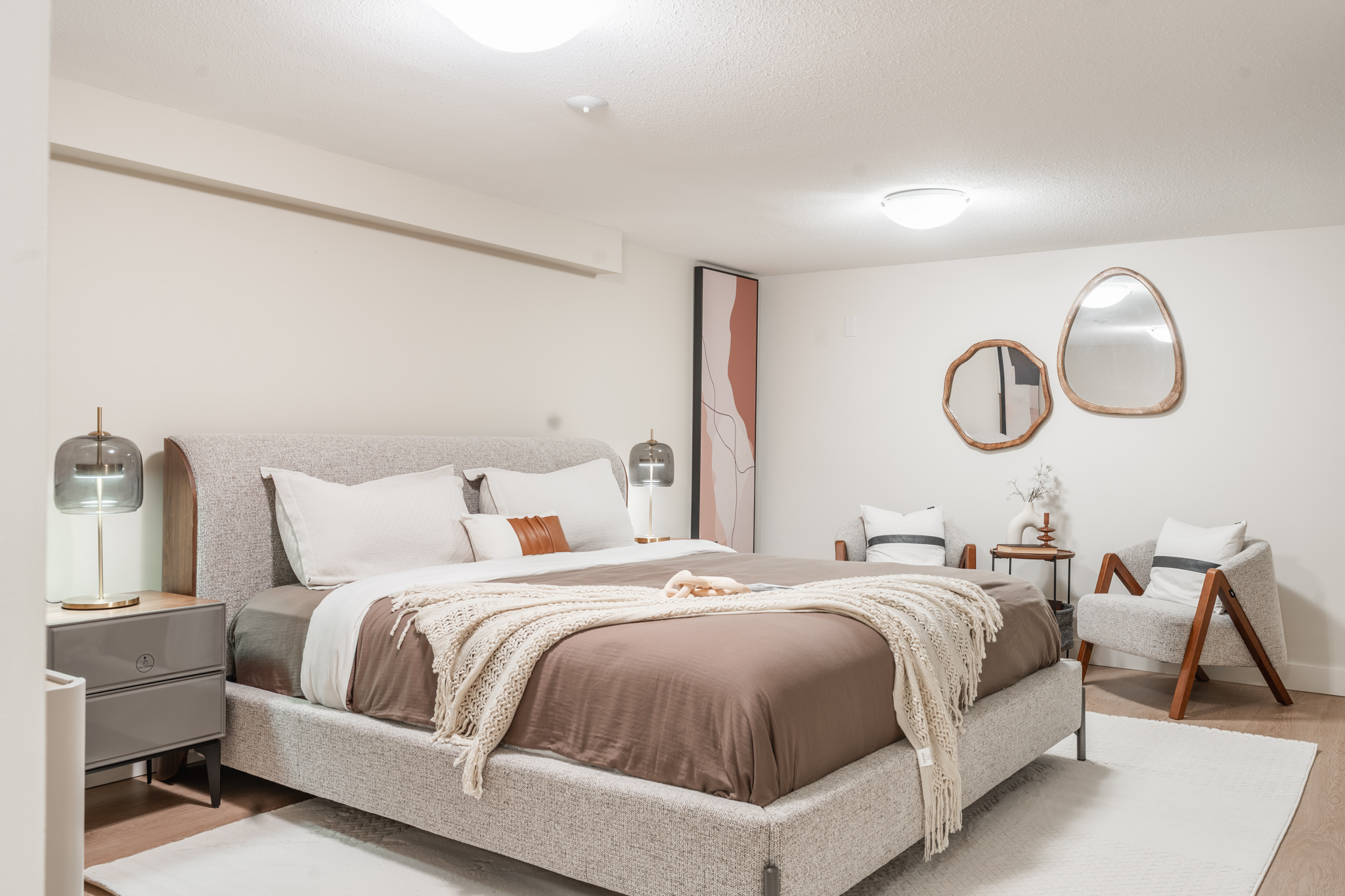 Warm neutral bedroom with upholstered bed, layered textiles, and modern seating